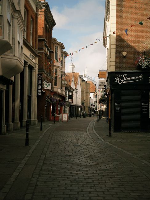 Exterior view of a retail shop on Southfields high street displaying a variety of cleaning tools and supplies, including brooms, mops, buckets, and plastic storage containers, arranged outside the sto