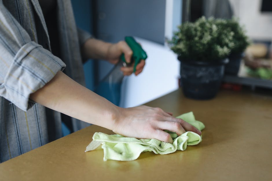 A light blue dustpan hangs on a plain white wall, with a wooden-handled brush inside it. The brush has beige bristles and is positioned with the handle facing upward, resting inside the dustpan. The s